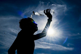Una persona se refresca con agua bajo un sol intenso, en medio de una jornada de calor extremo.